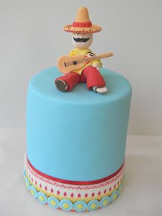 a blue cake with a small toy sitting on it's top and holding a guitar