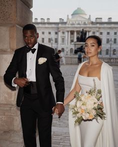 a bride and groom walking together in front of a large building with columns on either side