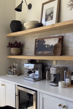 a coffee maker on top of a white counter next to shelves with pictures and other items