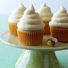 several cupcakes with white frosting on a cake platter and one has a small yellow toy