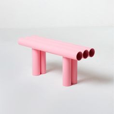 a pink bench sitting on top of a white floor next to two red pipes in the shape of three circles