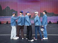 four young men standing in front of a stage wearing blue denim jackets and black pants