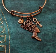 "This listing is for a Nefertiti and ankh charm bangle bracelet with a hand-stamped initial charm. This bracelet is adjustable, which makes it a great gift for someone if you don't know their wrist size. Just squeeze to adjust! :) One size fits most. You'll be able to choose your initial from the drop-down menu, and you can also choose to have these charms placed on a keychain or necklace instead. **Please see the second photo for charm scale. These are SMALL charms. This bracelet is made from metal alloy. The initial charm measures 5/16\". - - - - - - - If you'd like to add extra charms or birthstones to your item, just follow these links: ♥ EXTRA LETTER CHARMS: https://www.etsy.com/listing/231546815/add-a-letter-charm?ref=pr_shop ♥ EXTRA CRYSTAL BIRTHSTONES:  https://www.etsy.com/listing Adjustable Bronze Jewelry With Lobster Clasp, Symbolic Personalized Bracelets, Adjustable Nickel-free Bronze Bracelet, Symbolic Adjustable Bronze Bracelets, Adjustable Symbolic Bronze Bracelets, Adjustable Symbolic Bronze Bracelet, Adjustable Bronze Symbolic Bracelets, Personalized Brass Bracelets As Gift, Personalized Brass Bracelets For Gift