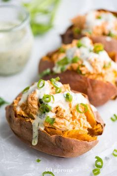 three baked potatoes with green onions and cheese on top, sitting on a white plate