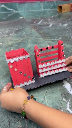 a person is making a model of a red fence and gate with beads on it