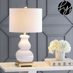 a white table with a lamp and flowers on it