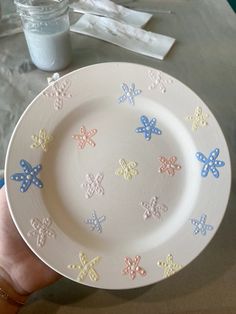 a hand holding a white plate with multicolored butterflies on it and a jar of milk in the background