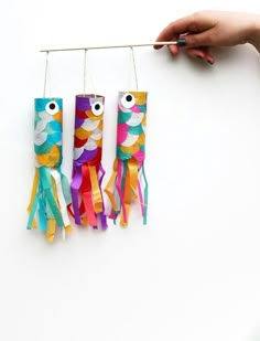 three fish made out of toilet paper hanging on a clothes line with one person's hand