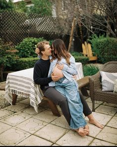 a man and woman sitting on a bench in the middle of a yard, kissing