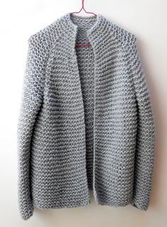 a gray knitted sweater hanging on a white wall next to a red hanger