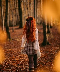 a woman with red hair is walking through the woods