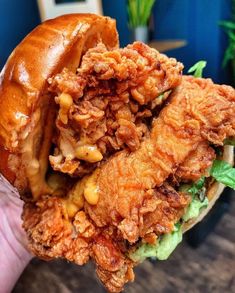 a hand holding a chicken sandwich with lettuce and sauce on it's bun