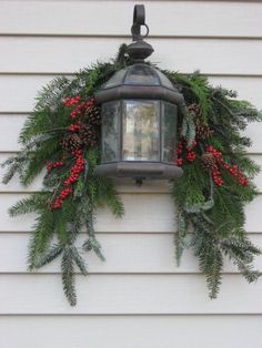 a lantern hanging from the side of a house decorated with christmas greenery and berries