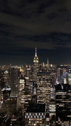 the city skyline is lit up at night with skyscrapers in the foreground and dark clouds overhead