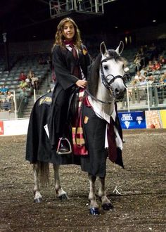 a woman riding on the back of a white horse in an indoor arena at night