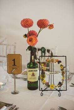 a table with flowers, wine bottle and place card holders on it for guests to sit at