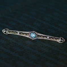 A delicate and beautiful filigree bar brooch by American jewellers Wordley, Alsopp & Bliss. Crafted in 14ct gold topped with platinum, it is set with a fiery blue zircon flanked by 2 old-cut diamonds & decorated with open work filigree, milgrain and engraved foliate detail. AVAILABLE NOW AT Antique & Vintage Elegance, online jewellery. Free express postage Australia wide. #Zircon #BlueZircon #OldCutDiamond #AntiqueBrooch #AntiqueJewellery #ArtDecoJewellery #ArtDecoBrooch #Filigree Bar Brooch, Art Deco Brooch