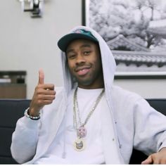 a man in a white hoodie giving the thumbs up while sitting on a couch