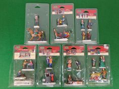 five action figures in plastic packaging on a green tableclothed surface, including one man and the other woman