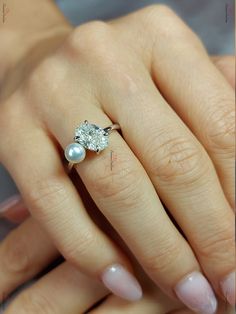 a close up of a person's hand with a ring on their finger and a pearl in the middle