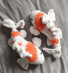 three crocheted koi fish are laying on a bed together, one is orange and the other is white