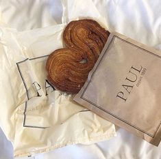 a bagel sitting on top of a white bed next to a brown paper bag