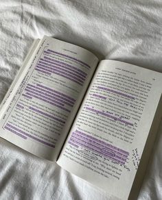 an open book sitting on top of a bed next to a white sheet with purple writing