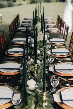 a long table set up with place settings and black candles for an elegant dinner party