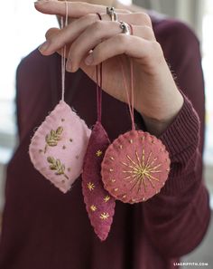 a woman holding three ornaments in one hand and two on the other with gold thread