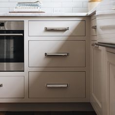 an oven in the middle of a kitchen with white cupboards and drawers on both sides