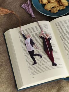 an open book sitting on top of a table next to a plate with cookies and other food