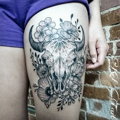 a woman's thigh with flowers and a bull skull tattoo on the side of her leg