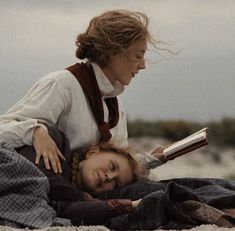 a woman reading a book to a child laying on the ground