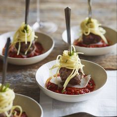 four small white bowls filled with meatballs covered in sauce and noodles on top of a wooden table