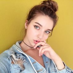 a young woman wearing a denim jacket poses for the camera with her hand on her chin