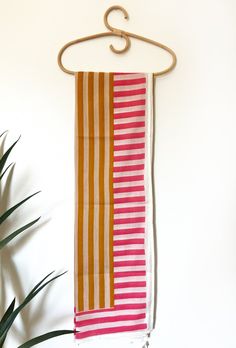 an orange and pink striped towel hanging on a wall next to a potted plant