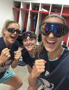 three women wearing ski goggles and smiling for the camera in front of a locker