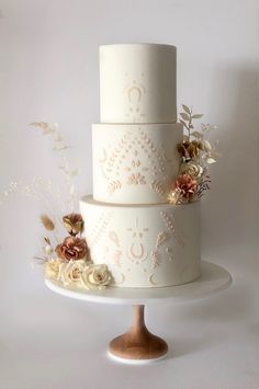 a three tiered wedding cake with flowers on the top and bottom, sitting on a pedestal