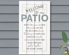 a wooden sign that says welcome to our patio on the side of a gray house