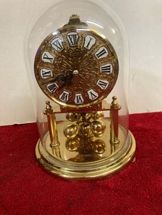 an antique clock under a glass dome on a red carpet