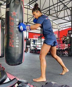 a woman in blue shirt and shorts boxing with punching bag next to her on the ground