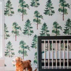 a teddy bear sitting next to a crib in front of a wall with trees on it