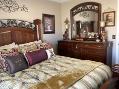 a large bed sitting under a mirror next to a wooden dresser and chest of drawers