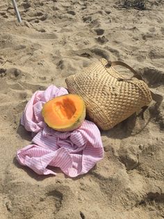 a piece of fruit is laying in the sand next to a straw bag and towel