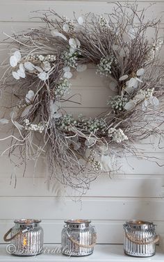 a wreath is hanging on the wall next to two mugs with flowers in them