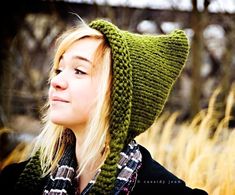 a woman wearing a green knitted hat and scarf in front of some tall grass