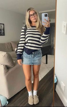 a woman taking a selfie in her living room wearing a striped sweater and denim skirt