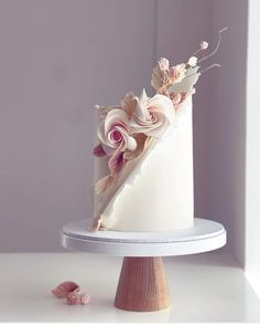 a white wedding cake with pink flowers and leaves on top, sitting on a stand