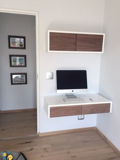 a white desk with a computer on top of it in front of a wall mounted monitor