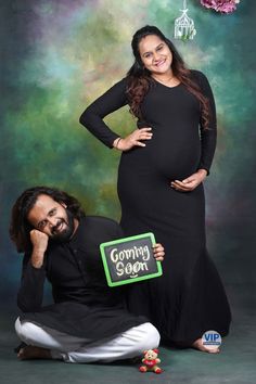 a pregnant woman and man pose for a photo in front of a green backdrop with the words coming soon written on it